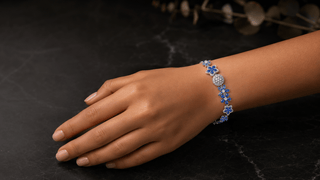 Hand wearing a blue and silver bracelet on a dark surface